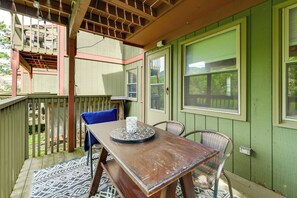 Una terraza de madera con una mesa y sillas, una alfombra estampada y una pared verde con ventanas.
