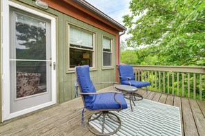 A wooden deck with two blue chairs and a small table, a sliding glass door, and a view of trees.