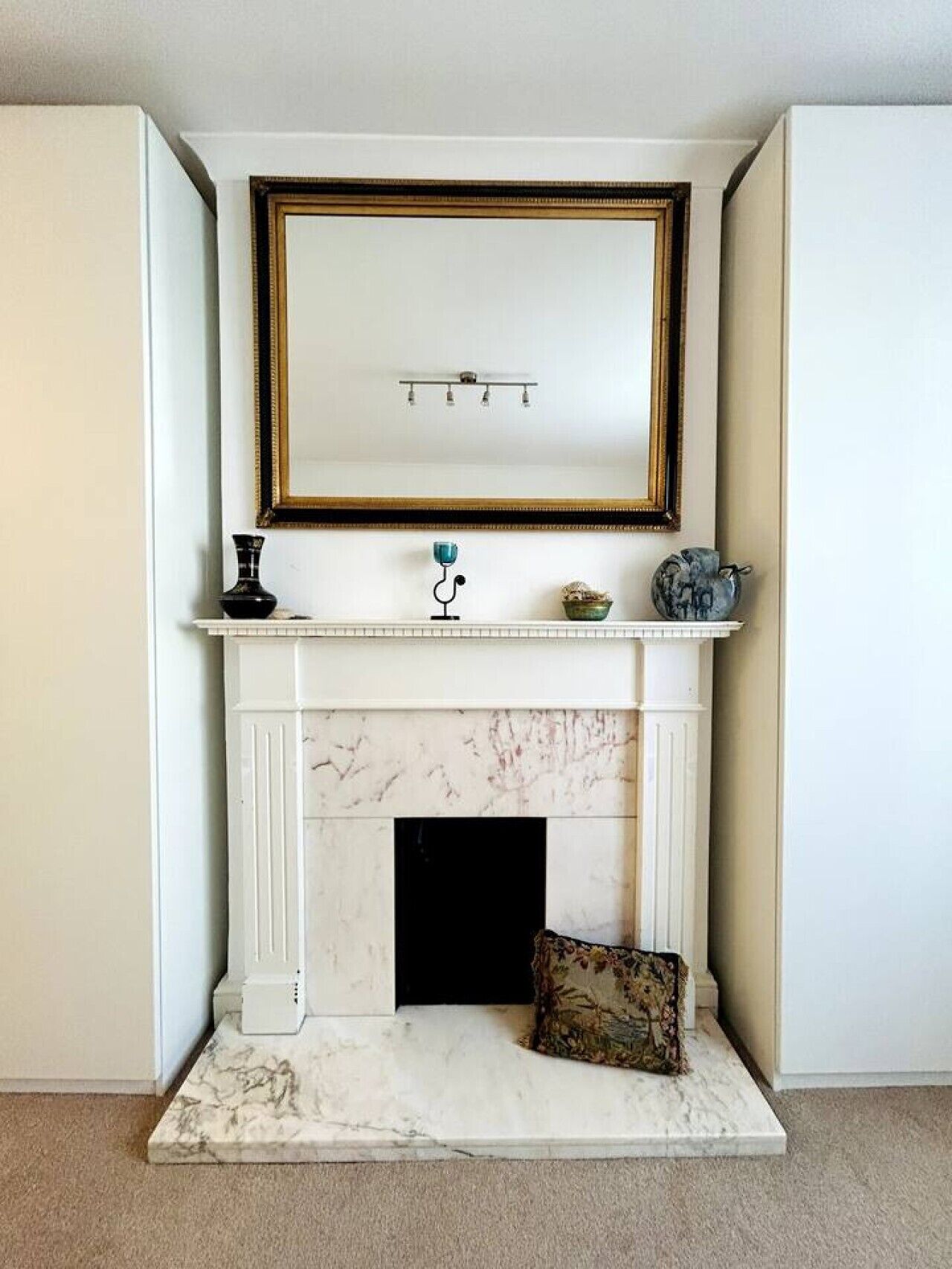 A white fireplace with a marble surround, a framed mirror above it, and a small table with decorative items.