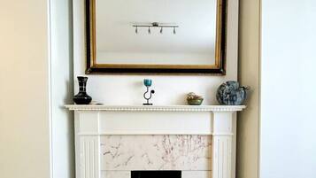 A white fireplace with a marble surround, a framed mirror above it, and a small table with decorative items.