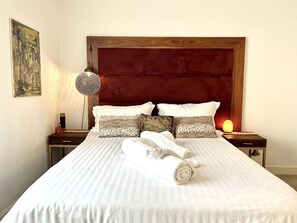 A neatly made bed with rolled towels, a wooden headboard, and a wall-mounted lamp.