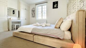 A bedroom with a bed, a vanity with a mirror, a window, and a wall with a decorative panel.