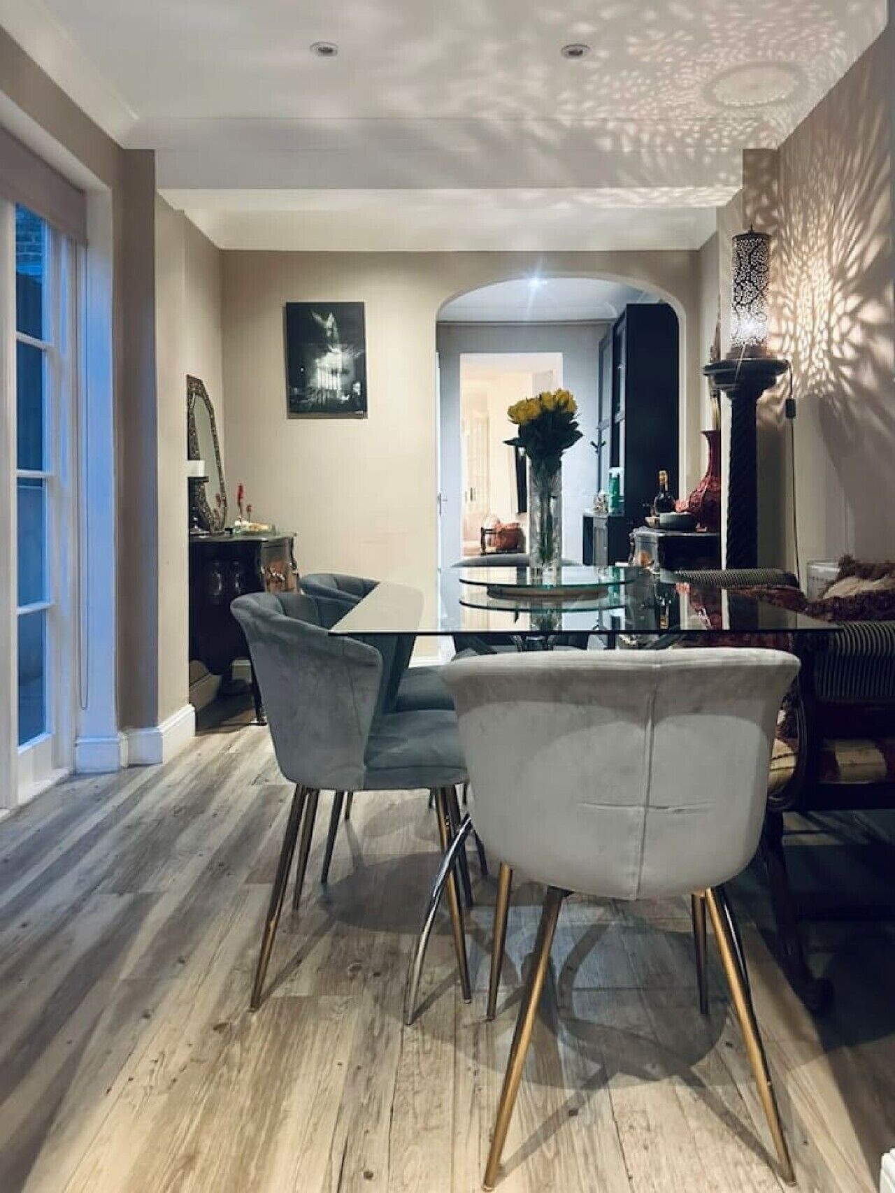 Een eethoek met een glazen tafel, gestoffeerde grijze stoelen en een houten vloer.