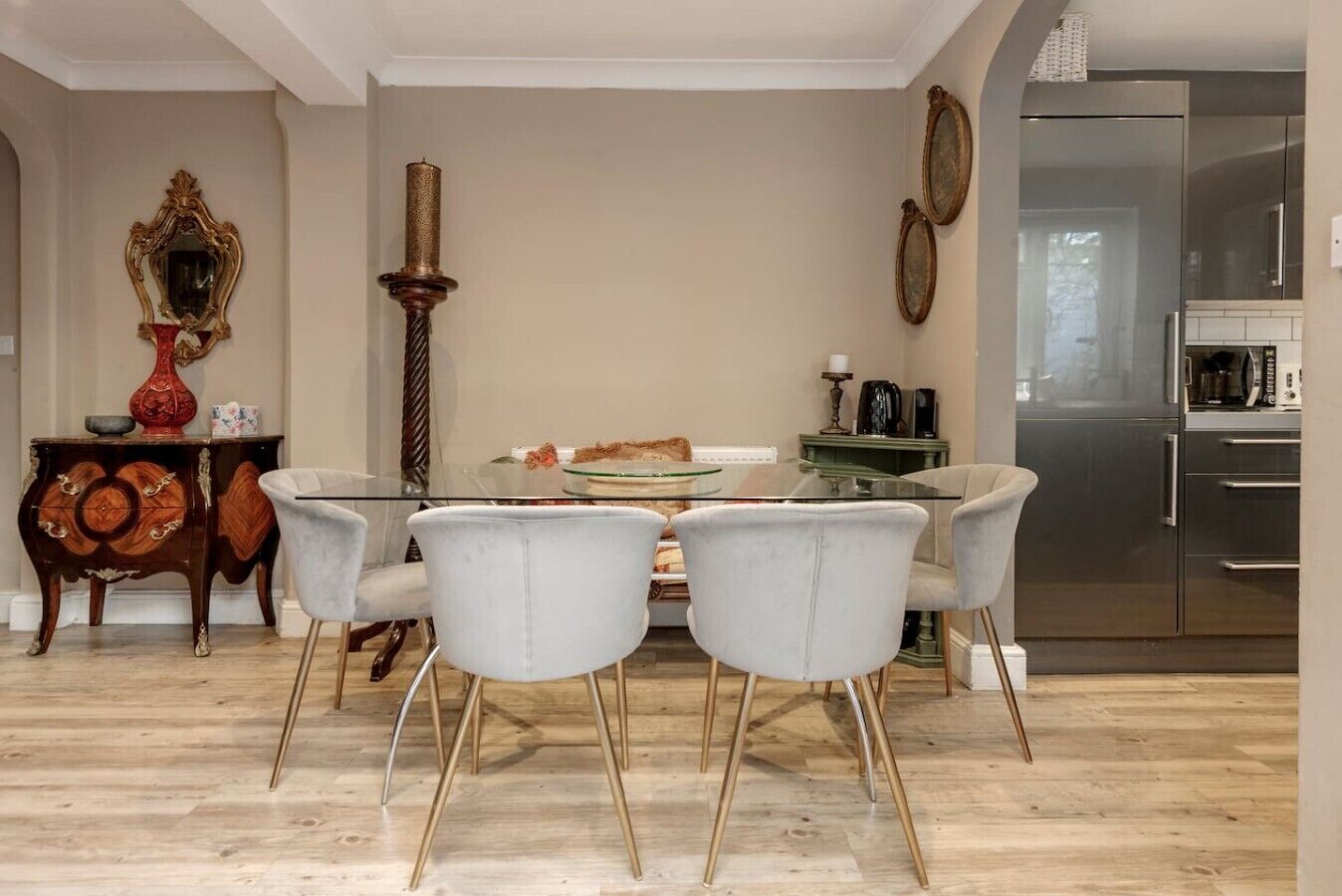 A dining area with a glass table, four chairs, a vase, a mirror, and a tall candle.