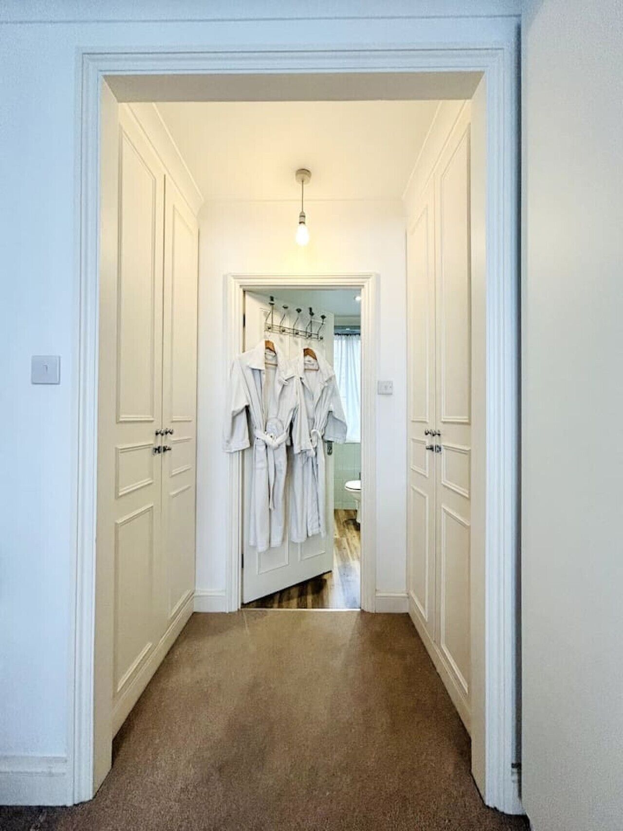 A hallway with white doors, a light fixture, and a rack of white robes.