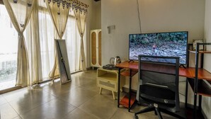 A room with a desk, a computer monitor, a chair, and a window with curtains.