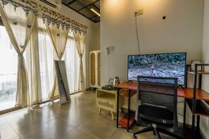 A room with a desk, a computer monitor, a chair, and a window with curtains.