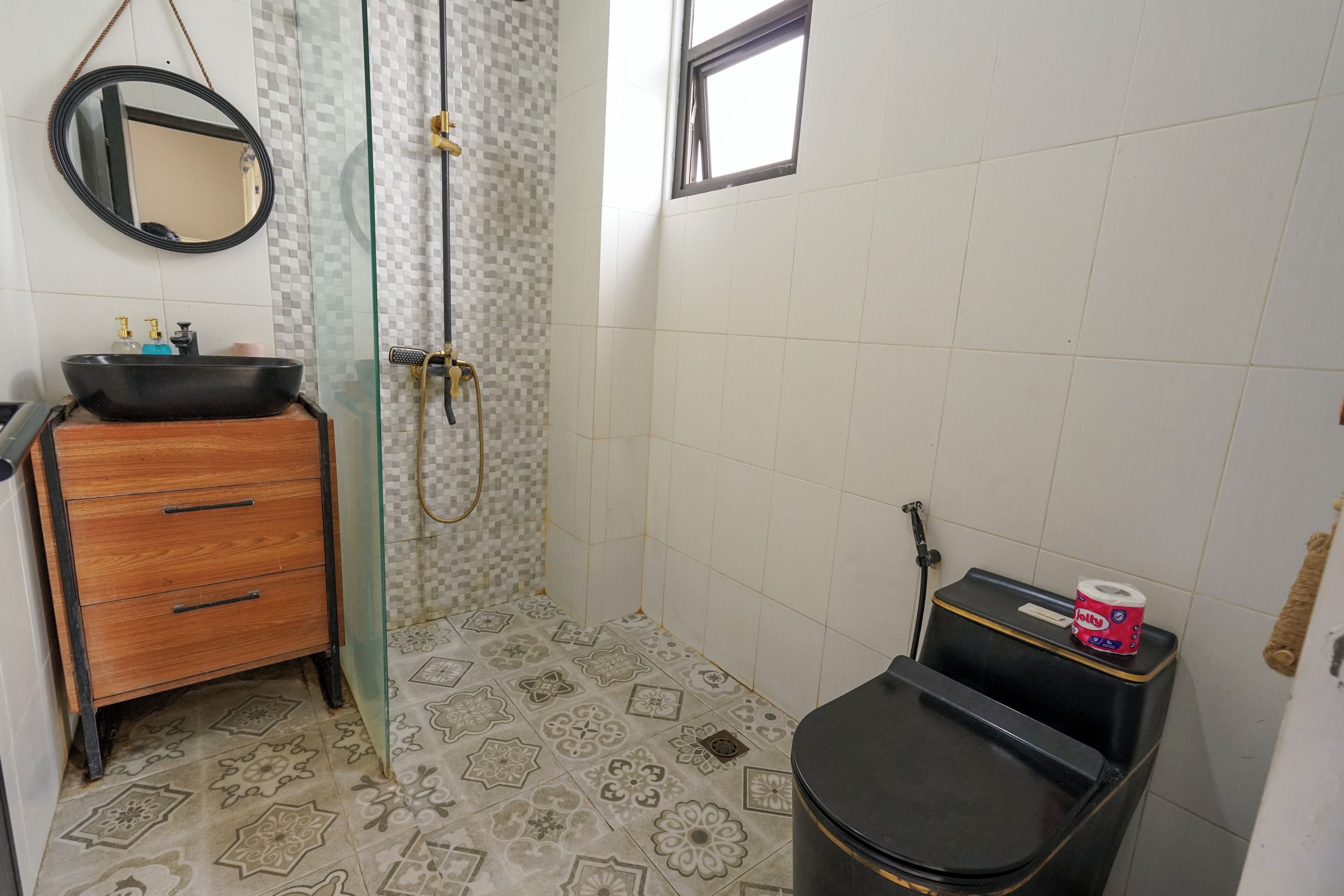 A bathroom with a wooden cabinet, a black sink, a glass shower enclosure, and a toilet with a roll of toilet paper.