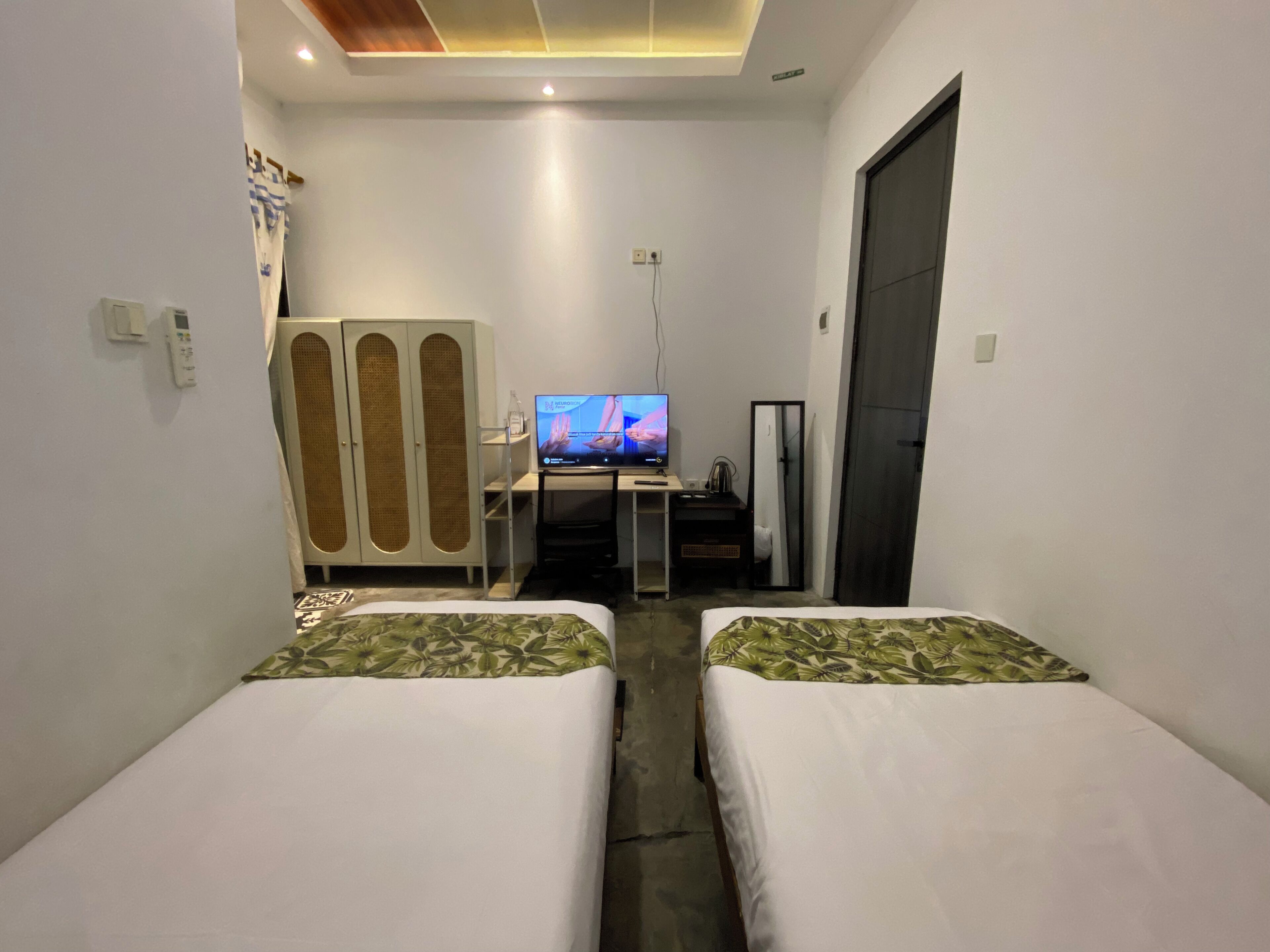 Ein Hotelzimmer mit zwei Betten, einem Fernseher, einem Schreibtisch mit Computer und einem Kleiderschrank.