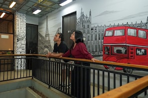 Un mural que muestra un autobús de dos pisos y un edificio con una aguja, visto desde un balcón con barandilla de metal.