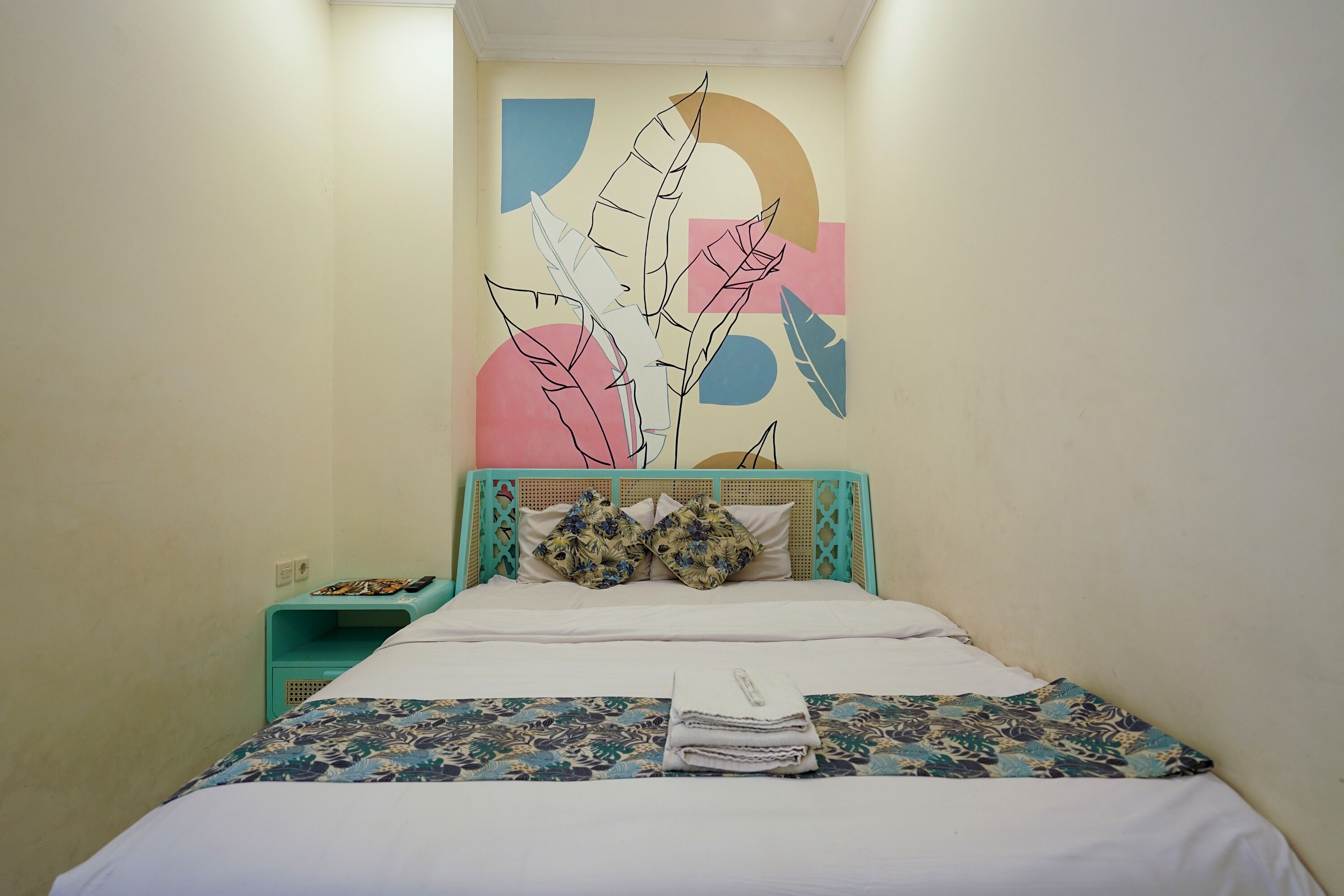 A single bed with a floral-patterned bedspread, a headboard with a geometric design, and a wall with abstract art.