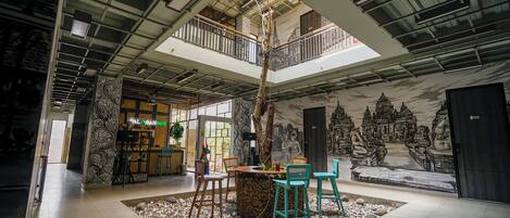 A spacious indoor area with a high ceiling, a central seating area with chairs, a small table, and a decorative tree.