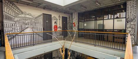 A multi-level atrium with a skylight, a staircase, and a mural depicting a cityscape.
