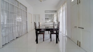 A spacious room with a dining table and chairs, a ceiling fan, and a large window with curtains. - Super Collection O Kulathoor Technopark (Thiruvananthapuram)