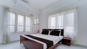 A bedroom with a wooden bed, white curtains, and a window with a view. - Super Collection O Kulathoor Technopark (Thiruvananthapuram)