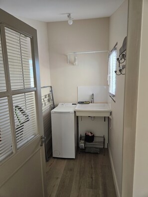 A compact laundry room with a washing machine, a sink, and a drying rack.