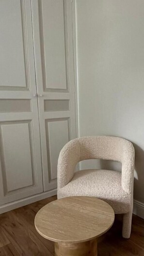 A room with a white wardrobe, a beige armchair, and a round wooden table. - Appartement Jehan de Beauce (Chartres)