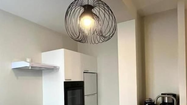 A modern kitchen with a black countertop, white cabinets, a black kettle, and a unique pendant light. - Appartement Jehan de Beauce (Chartres)