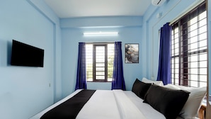Habitación de hotel con cama, televisión de pantalla plana en la pared y ventana con cortinas.