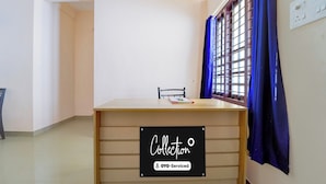 Una habitación con escritorio, una silla, un ventanal con cortinas azules y un letrero que indica 'Collection' y 'OYO-Serviced'.