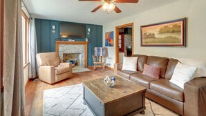 A living room with a fireplace, leather sofas, a coffee table, and a ceiling fan. - Peaceful Lake Getaway Near Bull Shoals Marina (Diamond City)