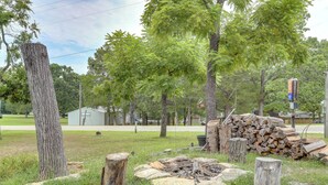 A rural outdoor setting with a fire pit, a stack of firewood, and a birdhouse amidst trees. - Peaceful Lake Getaway Near Bull Shoals Marina (Diamond City)