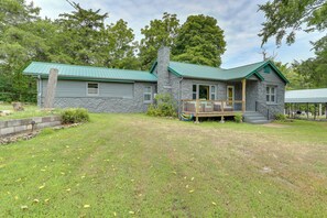 A stone house with a green roof, a porch with a bench, and a grassy yard. - Lake Getaway w/ Fire Pit Near Bull Shoals (Diamond City)
