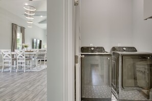 A laundry room with two Samsung washing machines, a dining area with a table and chairs, and a modern interior design. - 4 Mi to New Orleans! Extended Stay in Arabi (Arabi)