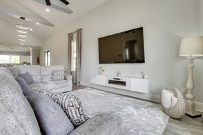 Ein modernes Wohnzimmer mit einem Ecksofa, einem flachbildfernseher an der Wand, einer weißen Unterhaltungsanlage und einem großen gewebten Pouf.