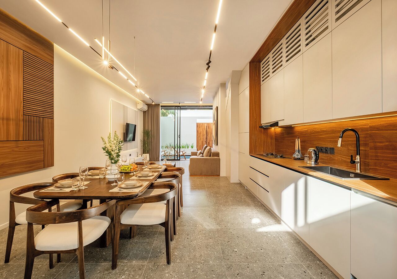 A modern kitchen with a dining area, wooden cabinetry, and a large window.