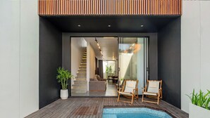 A modern outdoor pool area with a wooden deck, two lounge chairs, and a staircase leading to an interior space. - Elegant 2BR Private Pool Villa Umalas (Badung)