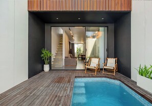 A modern outdoor pool area with a wooden deck, two lounge chairs, and a staircase leading to an interior space. - Elegant 2BR Private Pool Villa Umalas (Badung)