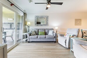 Una sala de estar con un sofá gris, un cojín verde, una lámpara blanca y un ventilador de techo.