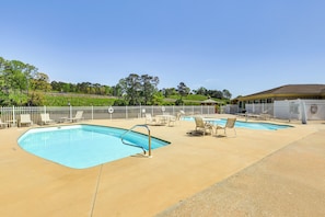 A swimming pool with lounge chairs and a covered seating area, surrounded by a fence and trees in the background. - Lake Martin Condo Getaway with Pool! (Alexander City)