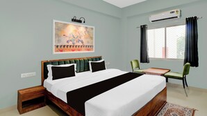 A bedroom with a bed, bedside tables, a desk, chairs, an air conditioning unit, and a window with curtains. - Super Collection O Udaipur City (Udaipur)
