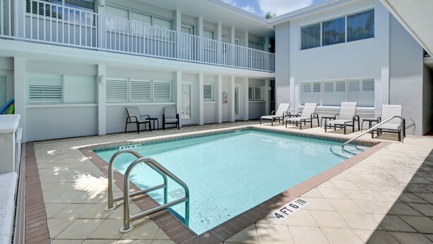A swimming pool with a 4 ft 6 in depth marker, surrounded by lounge chairs and a covered seating area with a view of the sky. - Walk to Beach! Old Naples Condo w/ Pool Access (Naples)