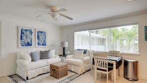 A living room with a white sofa set, a dining table with chairs, a ceiling fan, and artwork on the walls. - Walk to Beach! Old Naples Condo w/ Pool Access (Naples)