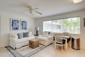 A living room with a white sofa set, a dining table with chairs, a ceiling fan, and artwork on the walls. - Walk to Beach! Old Naples Condo w/ Pool Access (Naples)