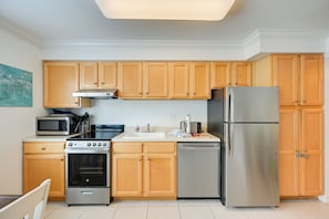 A modern kitchen with wooden cabinets, stainless steel appliances, and a tiled floor. - Walk to Beach! Old Naples Condo w/ Pool Access (Naples)