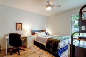 Een slaapkamer met een bed, bureau, stoel en een plafondventilator.