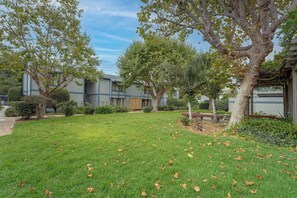 A residential area with a grassy lawn, trees, and a building with a blue and white exterior. - Walk to Capitola Village: Condo w/ 2 Surfboards (Capitola)