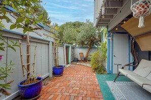 A narrow brick pathway leading to a seating area with a sofa and a table, surrounded by potted plants and a wooden ladder. - Walk to Capitola Village: Condo w/ 2 Surfboards (Capitola)