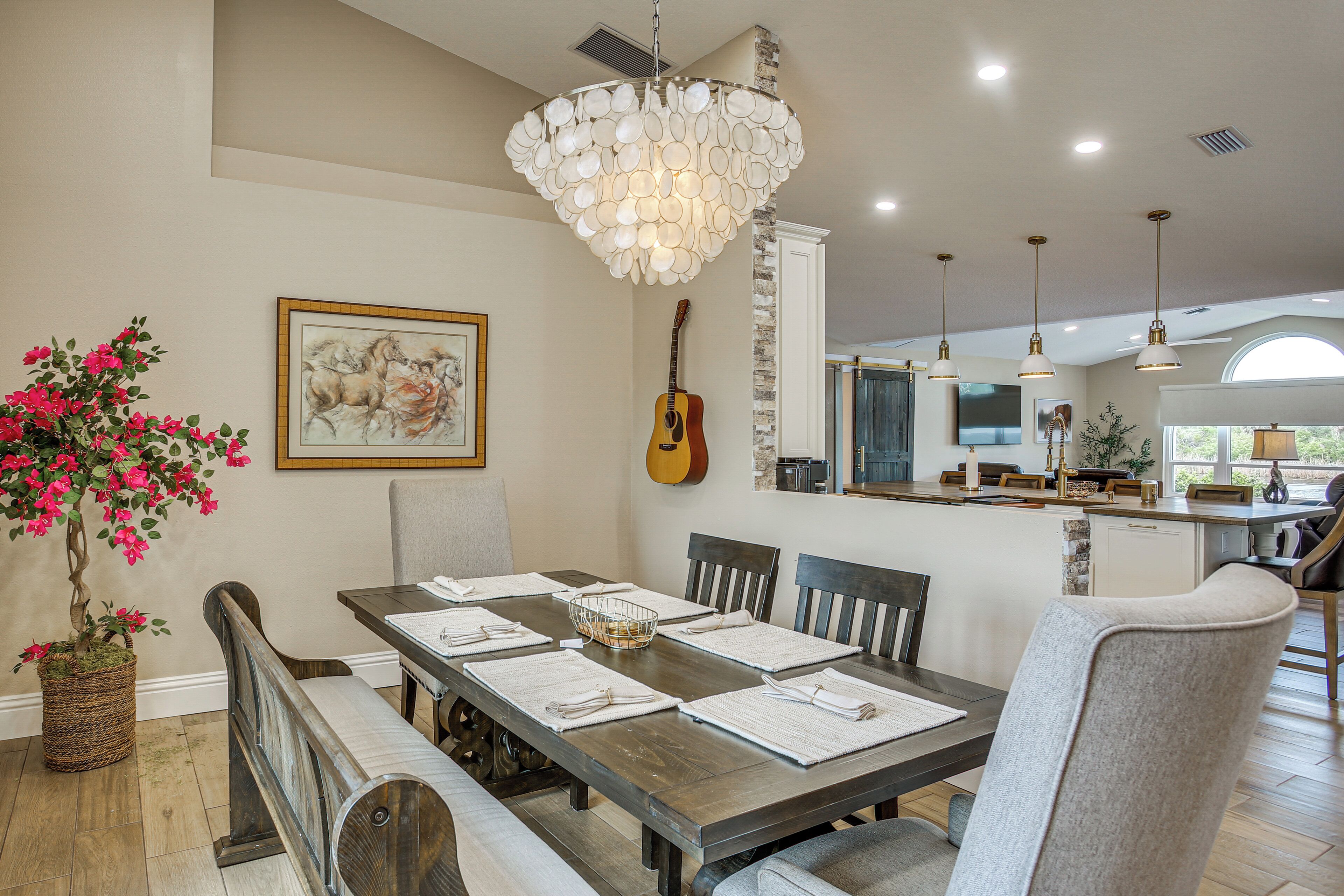 A dining area with a wooden table, chairs, a chandelier, a guitar, and a painting on the wall.