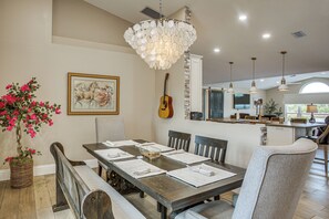 Un coin repas avec une table en bois, des chaises, un lustre, une guitare et un tableau accroché au mur.