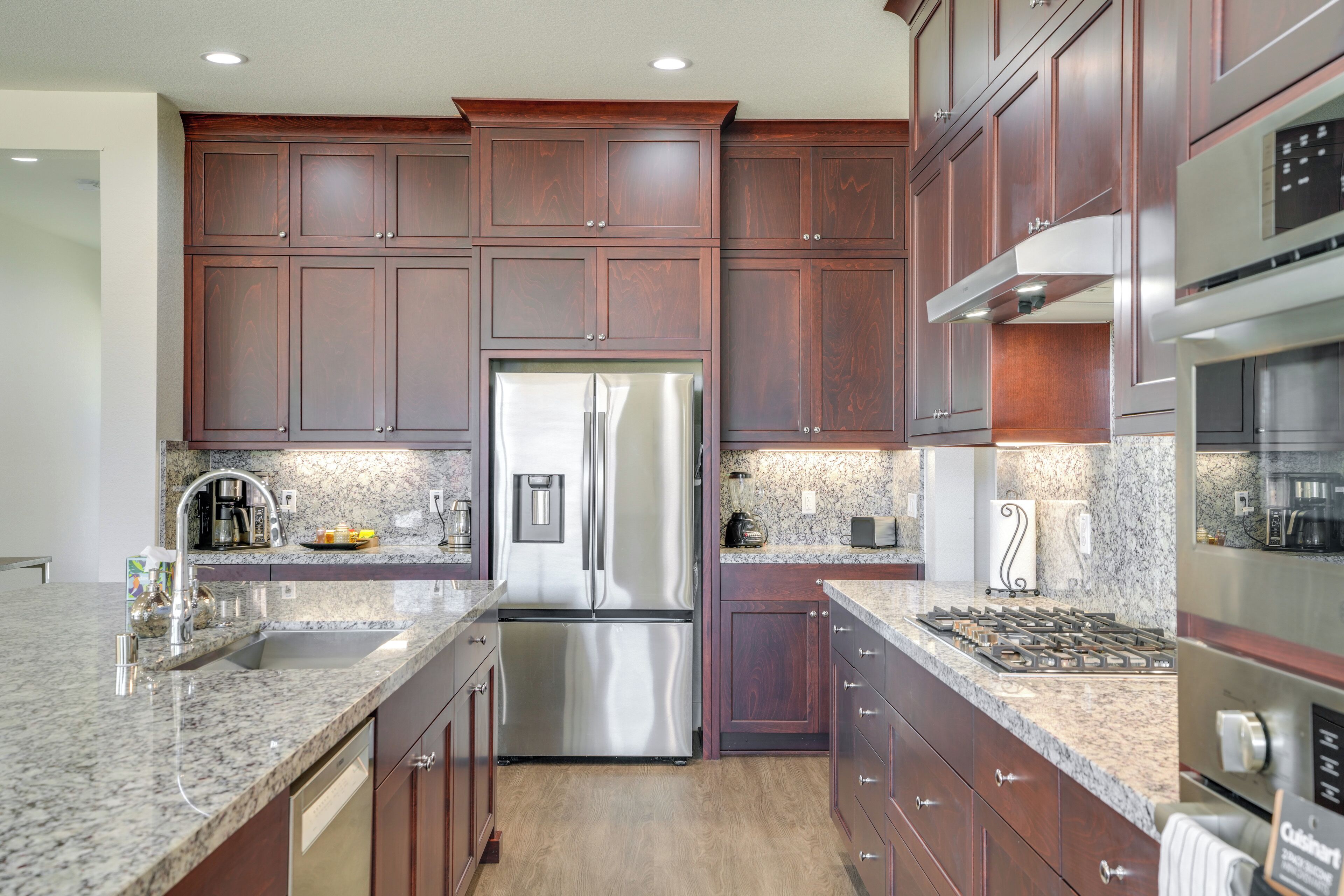 A modern kitchen with dark wood cabinets, stainless steel appliances, granite countertops, and a built-in oven.
