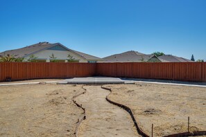A backyard with a wooden fence, a concrete pathway, and a dry, cracked ground. - Private Yard & Patio! Modern Manteca Gem (Manteca)