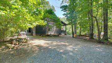 A rustic cabin with a gravel driveway, surrounded by dense trees.