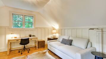 A room with a desk, chair, sofa, and a window with a view of trees.