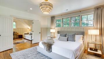A spacious bedroom with a large bed, a chandelier, and a view of trees through the window.