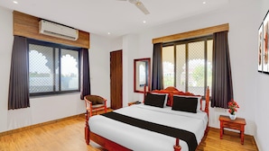 A bedroom with a bed, a chair, a nightstand, an air conditioning unit, and a ceiling fan. - Collection O RTO Office Udaipur (Udaipur)